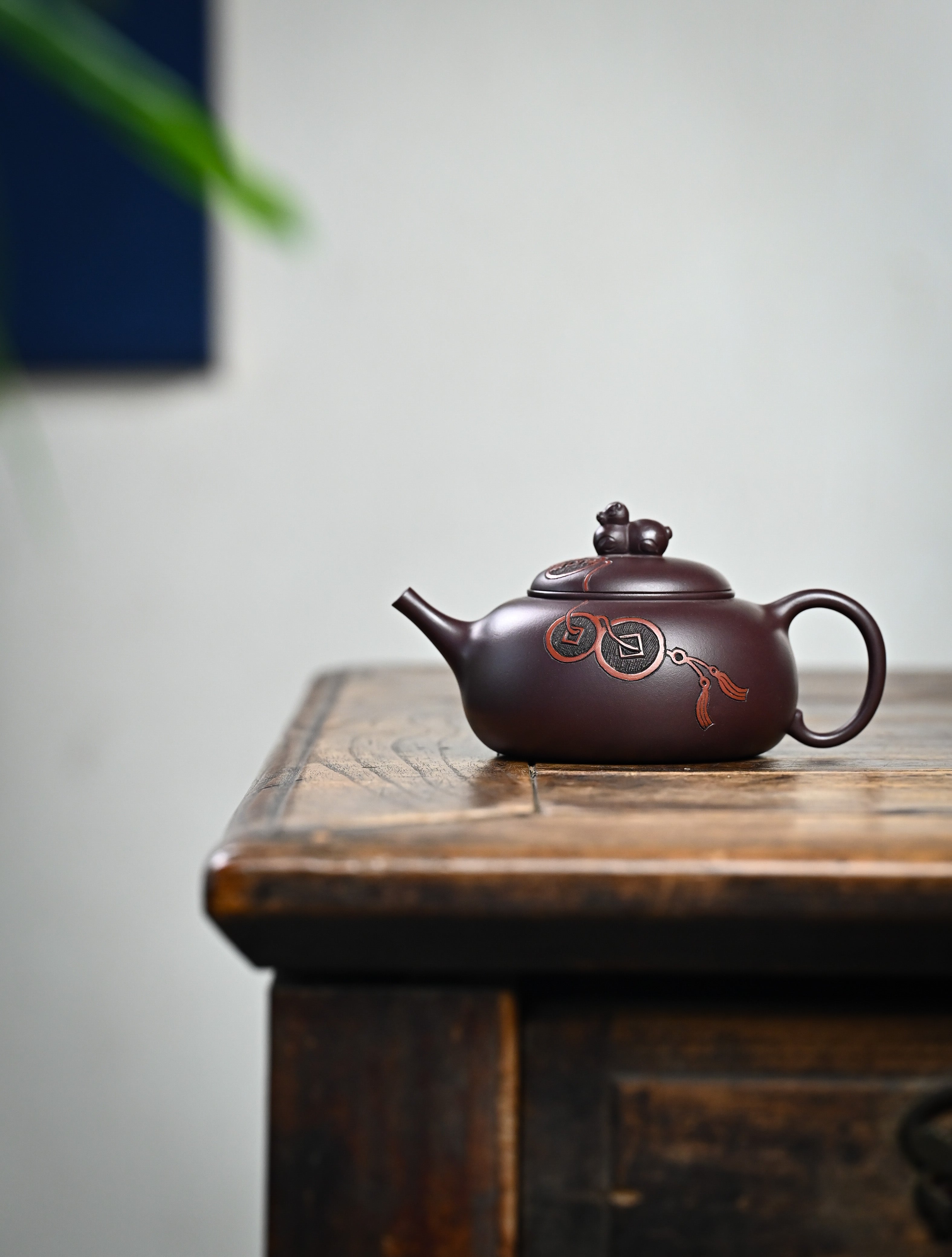 YANYOO handmade Yixing teapot featuring Zini clay and ancient Chinese coin sculpture, lifestyle wide-angle left side.