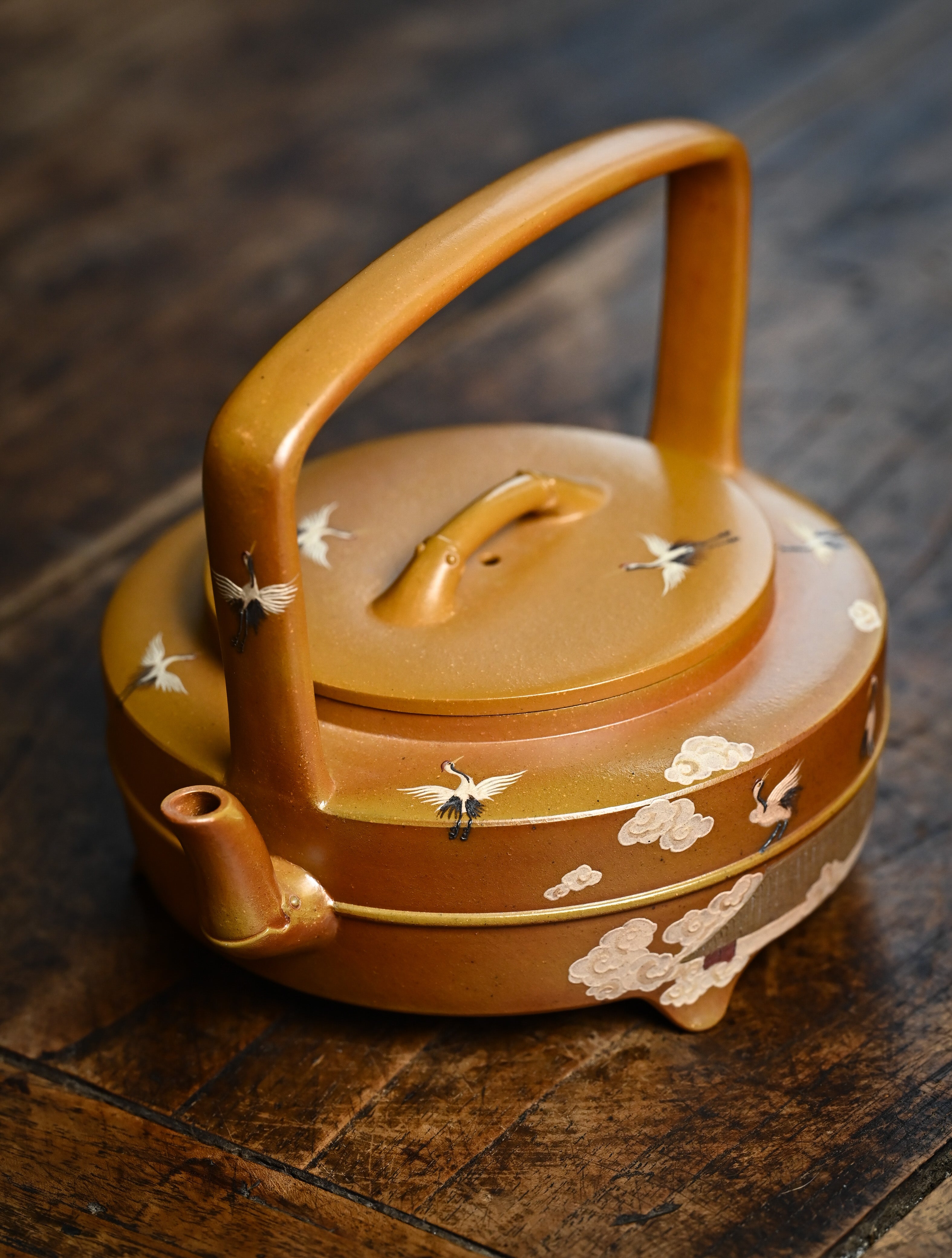 YANYOO handmade wood-fired Yixing teapot featuring hand-painted cloud-and-crane motif and lifting handle, lifestyle left side.