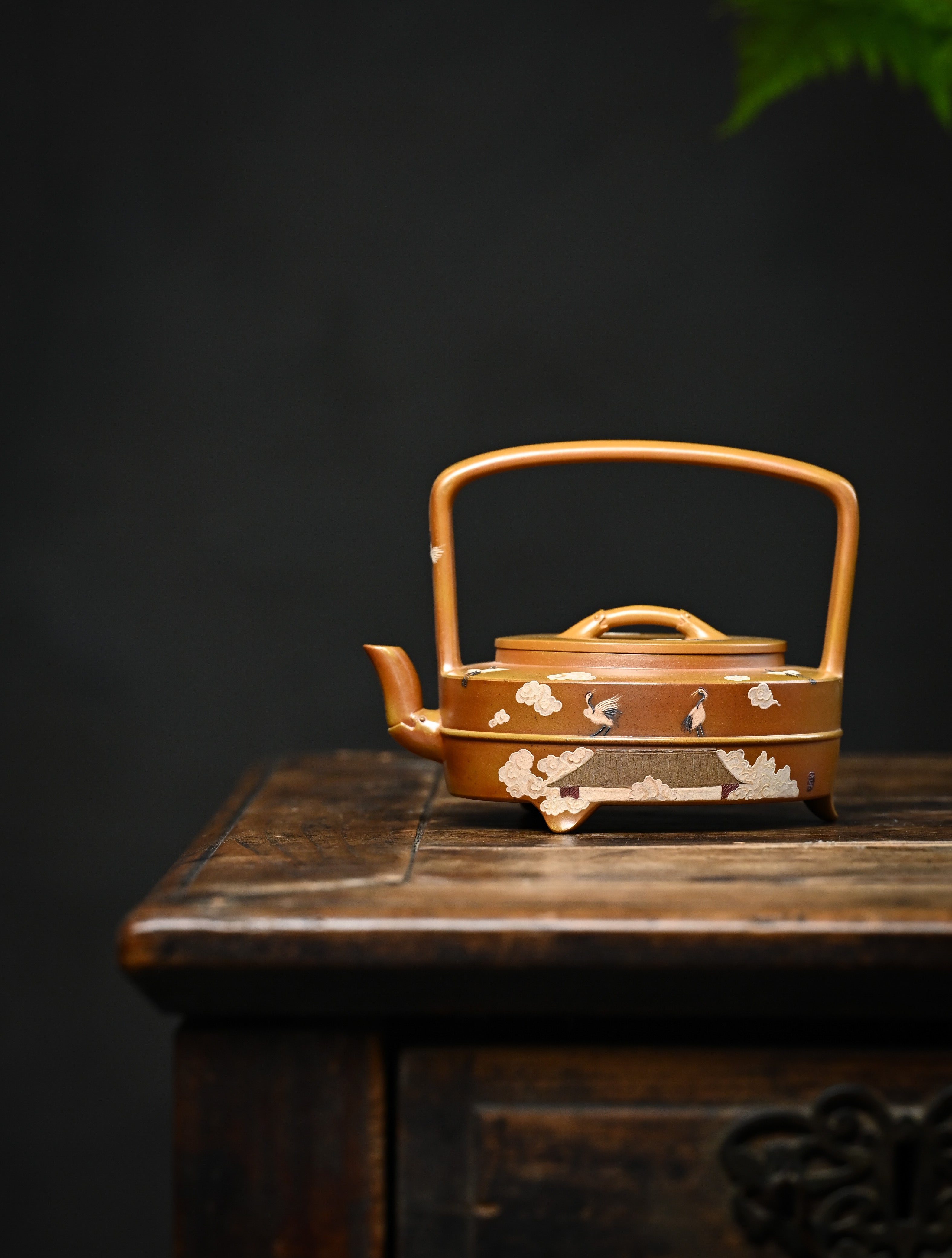 YANYOO handmade wood-fired Yixing teapot featuring hand-painted cloud-and-crane motif and lifting handle, lifestyle wide-angle left side.