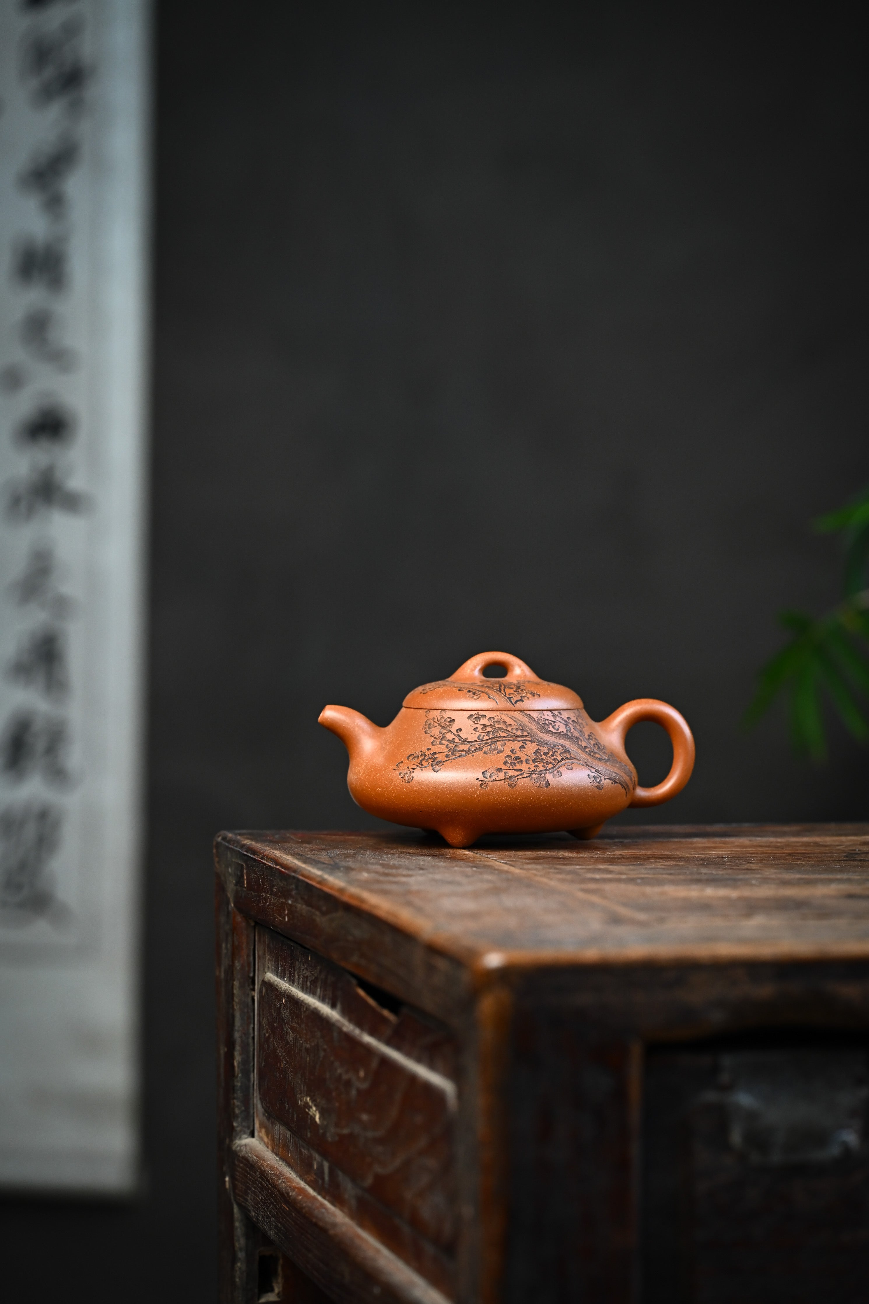 Handmade YANYOO Yixing teapot from Yu Cheng Kiln featuring aged Duanni clay and delicate engraving, lifestyle wide-angle left side.