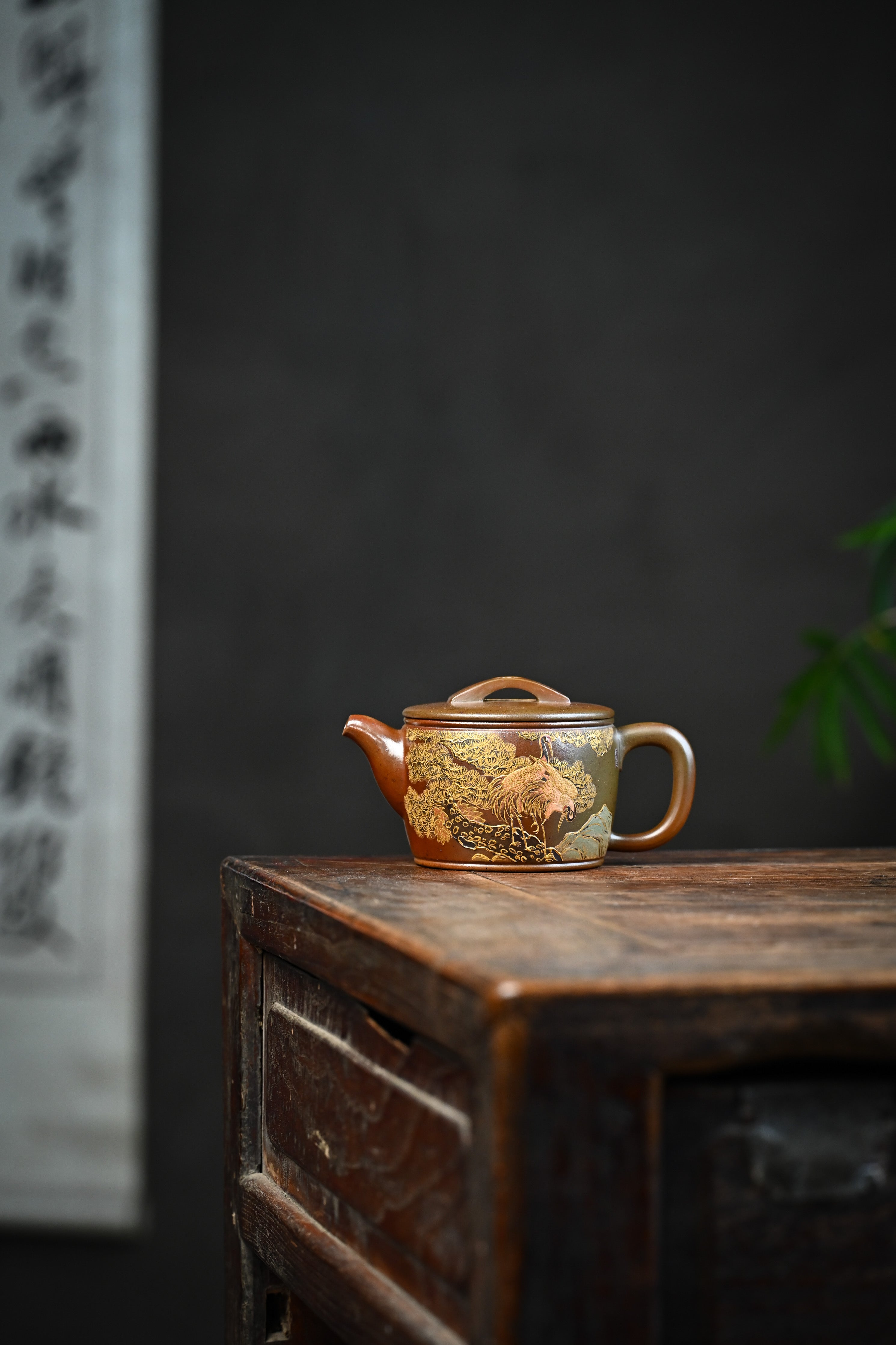 Handmade YANYOO Yixing teapot featuring hand-painted crane and gold enamel, lifestyle wide-angle left side.