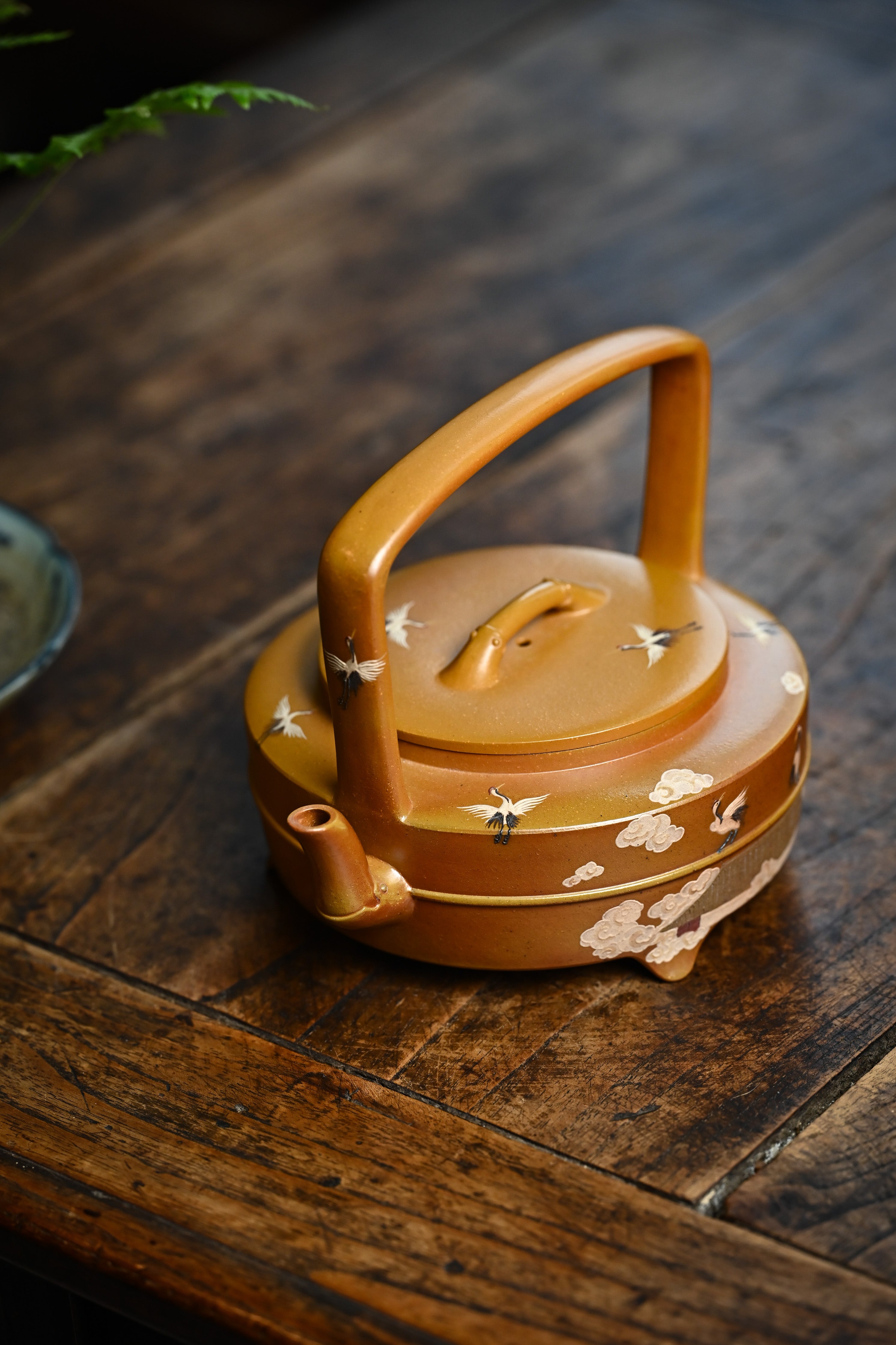 Handmade YANYOO Yixing teapot featuring hand-painted cloud-and-crane motif, lifestyle left side.