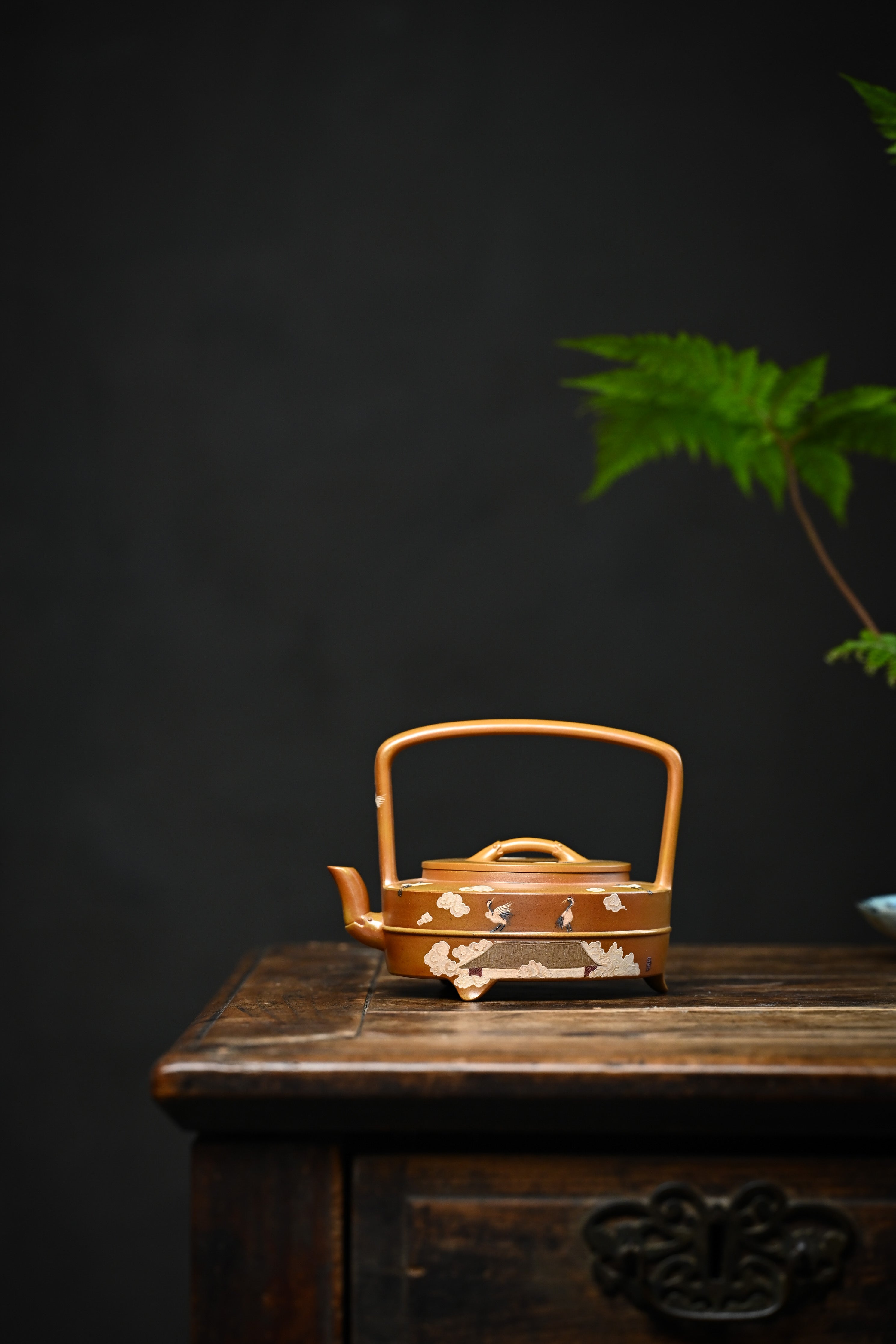 Handmade YANYOO Yixing teapot featuring hand-painted cloud-and-crane motif, lifestyle wide-angle left side.