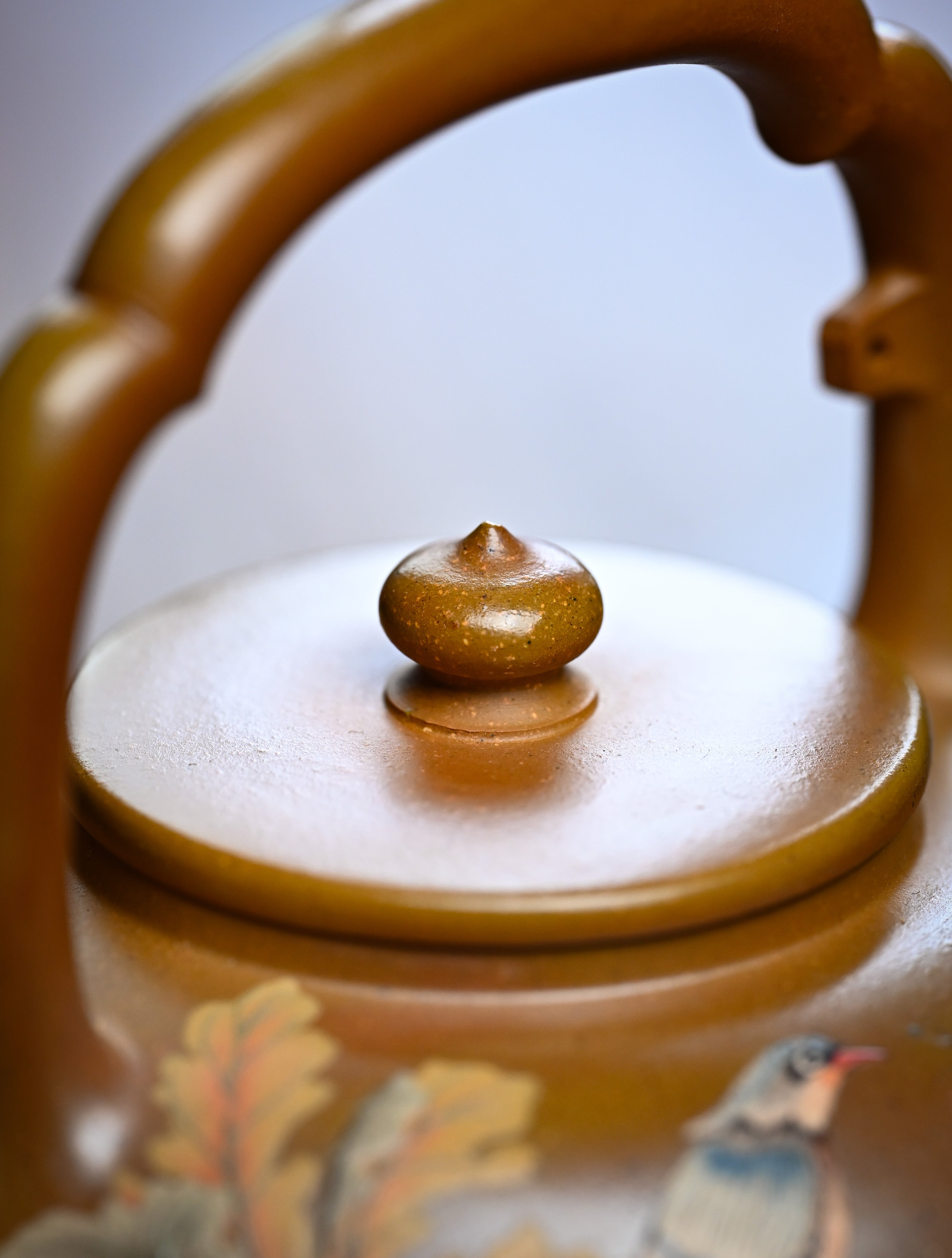 YANYOO handmade wood-fired Yixing teapot featuring hand-painted floral-and-bird motif and lifting handle, lifestyle detail top side.