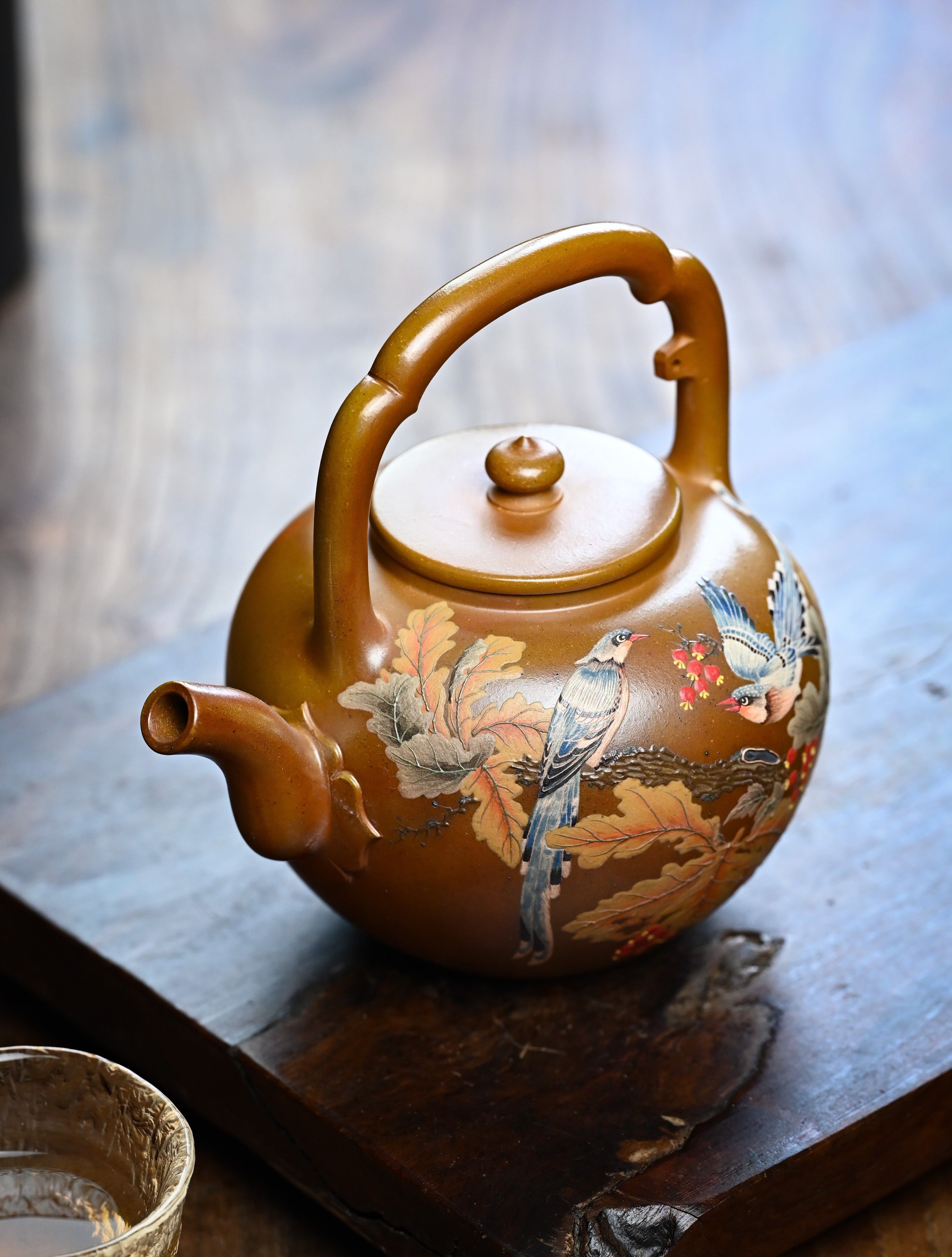 YANYOO handmade wood-fired Yixing teapot featuring hand-painted floral-and-bird motif and lifting handle, lifestyle left side.