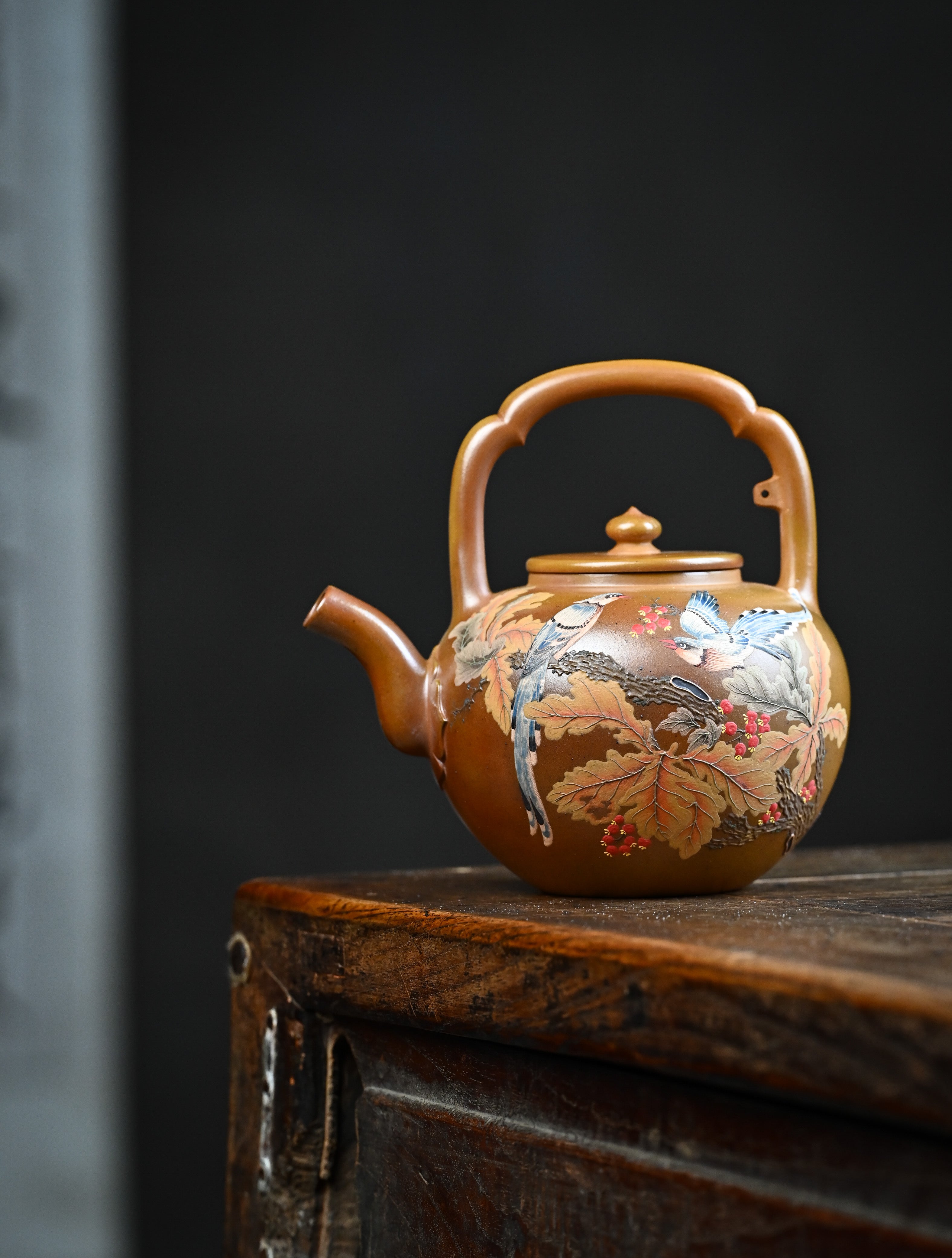 YANYOO handmade wood-fired Yixing teapot featuring hand-painted floral-and-bird motif and lifting handle, lifestyle wide-angle left side.