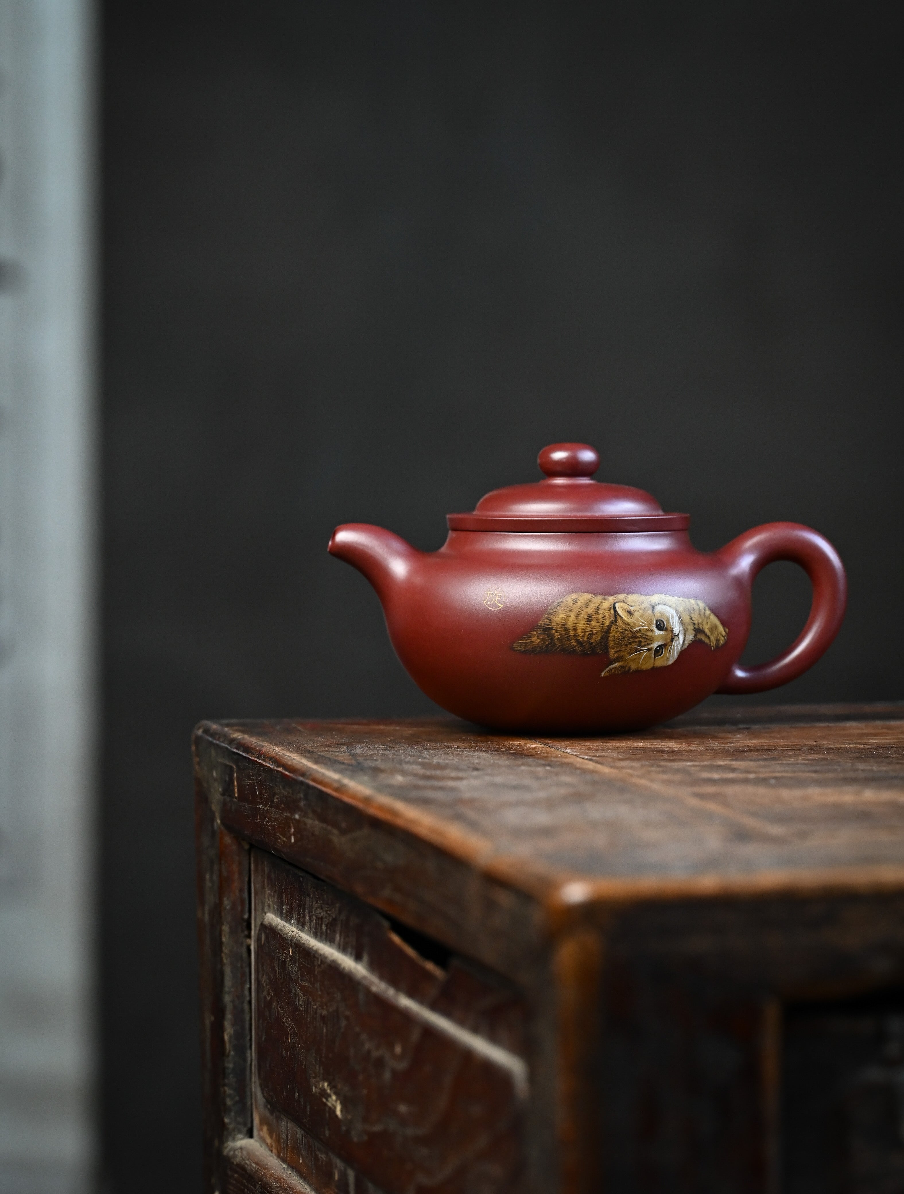 YANYOO handmade Yixing teapot featuring Hong Pi Long clay and embedded painting of cat by Master Xuanzi, lifestyle wide-angle left side.